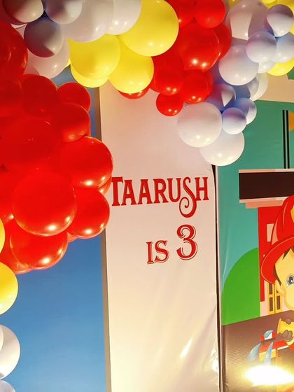 A close-up of a Fireman-themed backdrop, featuring a cartoon firefighter and a 'Taarush is 3' sign.