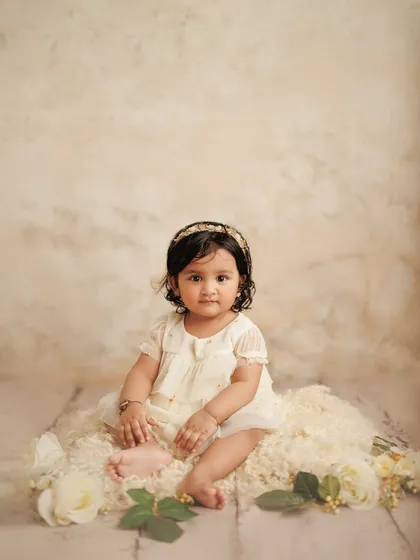 A full-length portrait of a baby girl celebrating her first milestone. The soft, neutral tones of the studio backdrop and her dress create a timeless and elegant image.