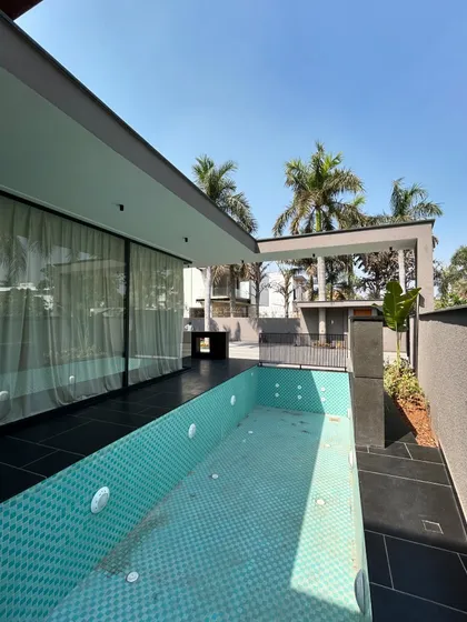 A view of the lap pool at Gulmohar Farmhouse, framed by modern architecture and lush palm trees. The design emphasizes clean lines and a strong indoor-outdoor connection.
