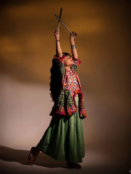 A vibrant and energetic shot celebrating culture. Dressed in a traditional outfit for Navratri, she strikes a powerful pose with dandiya sticks, showcasing her expressive capabilities.