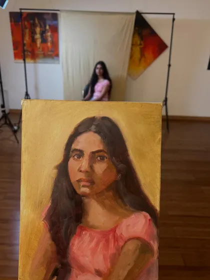 A shot of the live session with Simran, showing the painting on the easel and her posing in the background. These sessions are a collaboration between artist and model.