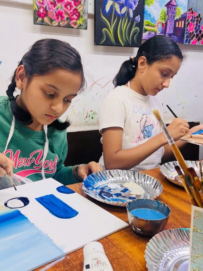 Concentration is key. Here, two young artists are focused on creating the perfect gradient for their sky and sea, an important first step in their landscape paintings.