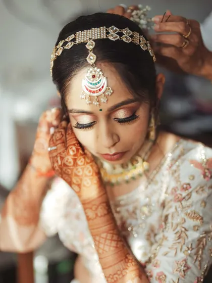 A close-up of the bride's final touches, her intricate matha patti being set in place.