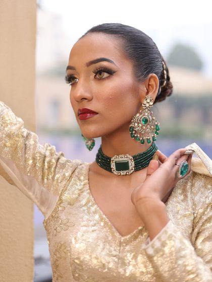 A close-up of the ivory lehenga look, focusing on the stunning green jewelry and flawless makeup.