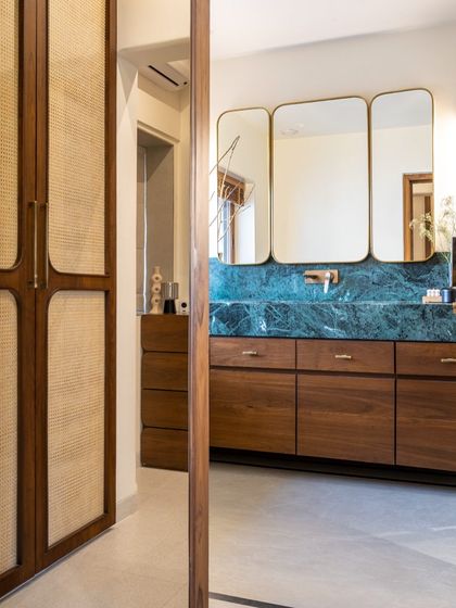 A seamless transition from the walk-in closet to the master bathroom. We used cane-paneled wardrobe doors to add natural texture, which contrasts beautifully with the bold green marble of the bathroom vanity visible beyond.