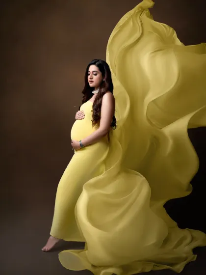 Grace and movement. The flowing yellow fabric of the gown creates a stunning visual effect in this artistic and elegant maternity portrait.