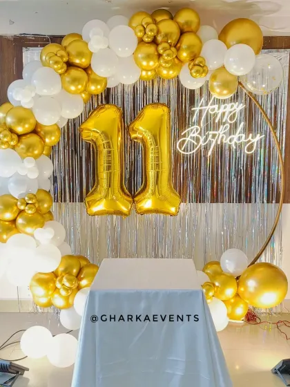 A glamorous 11th birthday setup with a silver tinsel backdrop. The circular frame is decorated with a white and gold balloon arch and large gold foil numbers.