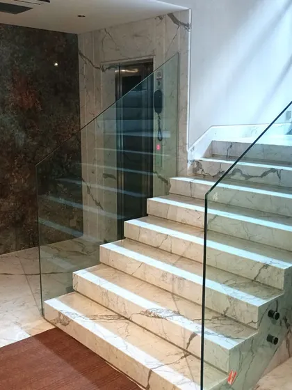 Another view of the side-mounted glass railing, showing its seamless integration with the luxurious marble steps and flooring.