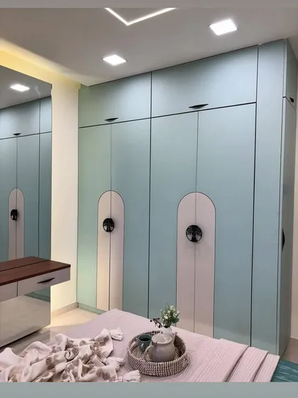 This custom wardrobe in a soft blue finish includes sleek, handleless doors and unique arched paneling, offering ample storage with a modern aesthetic.