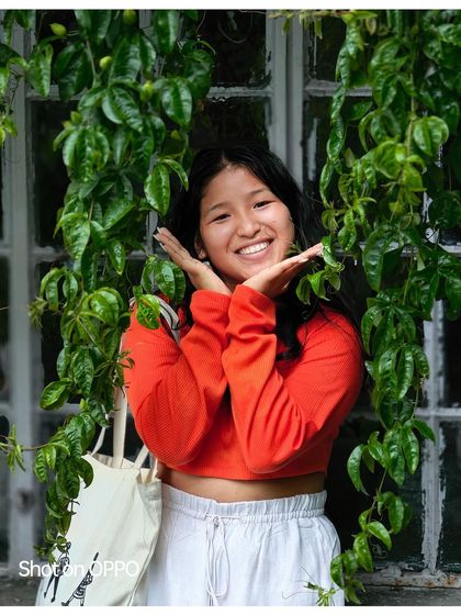 A joyful portrait of a young woman framed by lush green vines. Her radiant smile is the centerpiece of this vibrant, natural-light shot.