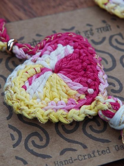 A close-up of the pink and yellow Lumba, showing the intricate heart-shaped crochet work and the touch of gold thread.