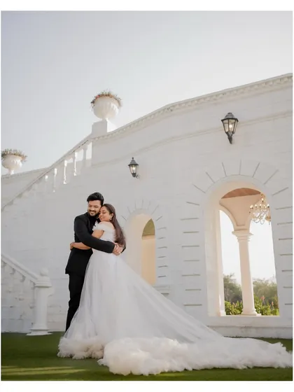 A full-length portrait of the couple against a grand white architectural backdrop. The bride's flowing gown adds a touch of drama to this pre-wedding photo.