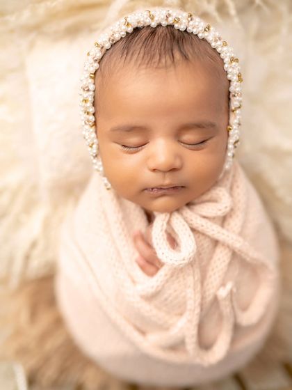 A close-up of a newborn princess in a delicate pink swaddle and pearl bonnet. So elegant and sweet.
