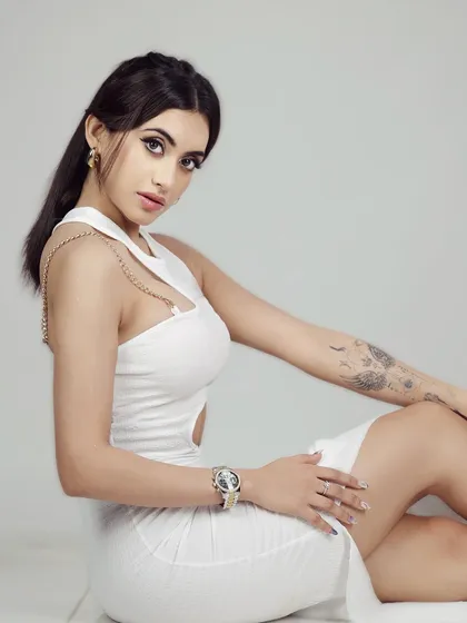 A confident seated portrait of the model in a white dress, looking directly at the camera.