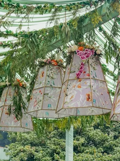 A dreamy canopy of hanging floral-printed lampshades and cascading greenery, creating a whimsical ceiling for an outdoor event.