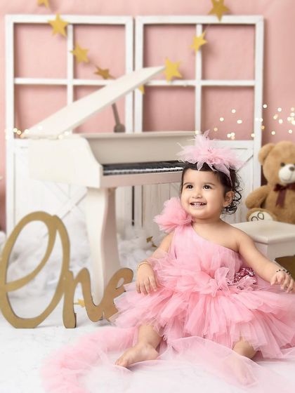 A pretty-in-pink princess. This little girl's fluffy pink dress and the soft, romantic studio setup with a white piano create a classic and beautiful birthday portrait.