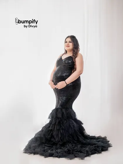 A full-length solo portrait showcasing the stunning black sequin gown. The simple white background makes the dress and the beautiful baby bump the true stars of the photo.