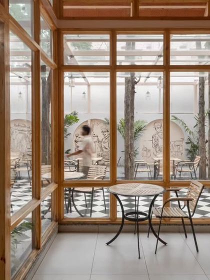 The design allows for a seamless flow from the enclosed cafe space to the outdoor seating area, which features a classic black-and-white checkered floor.