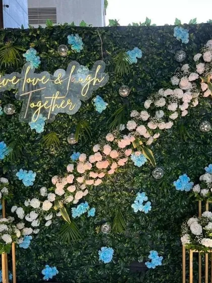 A beautiful selfie backdrop made of a green wall, decorated with a diagonal floral arrangement and a neon sign saying "Live love & laugh Together".