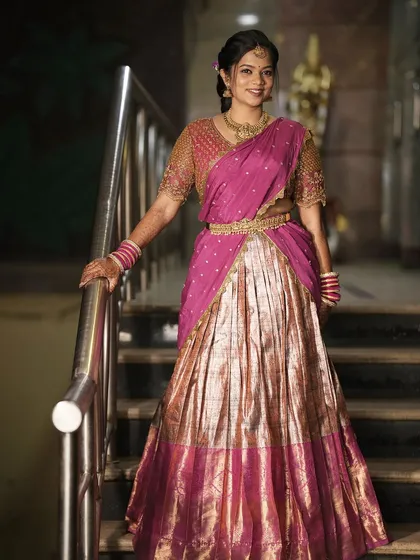 A stunning engagement look featuring a pink and gold half-saree. The makeup is glamorous yet traditional.