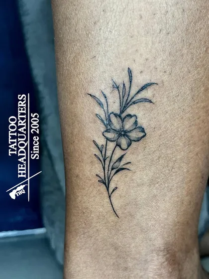 A minimalist flower tattoo on the leg, featuring a single bloom on a delicate stem.