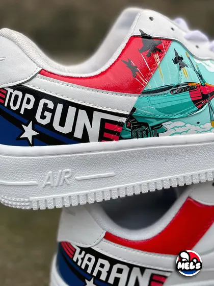 A detailed shot of the 'Top Gun' logo and fighter jet artwork on our custom Nike sneakers. The jet is shown in action against a teal sky with red accents.