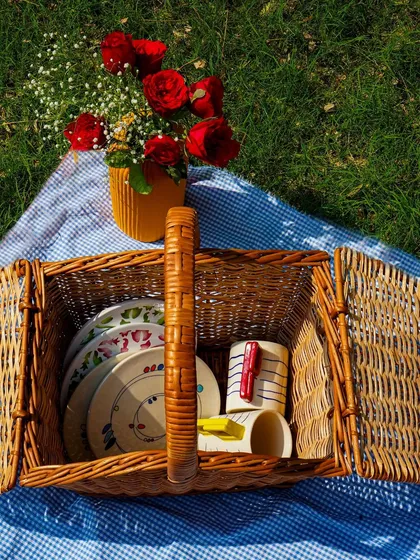 A classic picnic basket filled with colorful, artisanal plates and mugs, set on a gingham blanket. This image evokes a sense of nostalgia and outdoor fun.