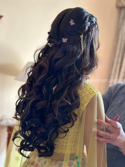 A back view of a romantic half-up style with a waterfall braid and scattered butterfly clips, ideal for a whimsical Mehendi look.