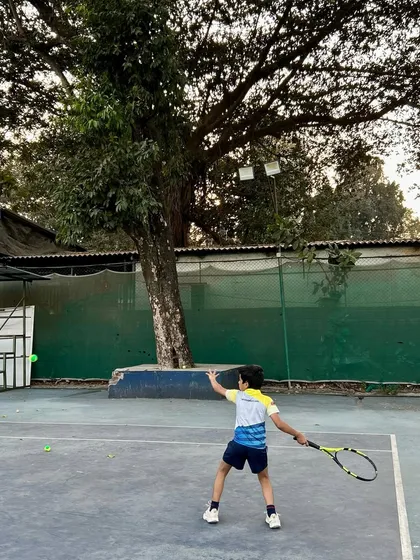 A young player hits a backhand with determination, framed by the trees and the court.