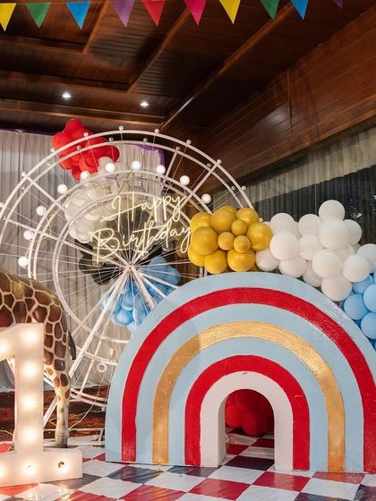 A fun photo corner at Dhiren's carnival party, with a large giraffe prop, a rainbow arch, and a light-up number '1'.