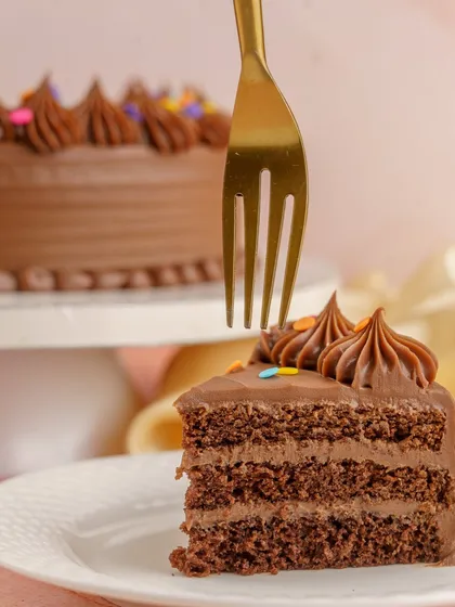 A perfect slice of the Milk Chocolate Birthday Cake, showing the rich layers of sponge and ganache. It's the sweet slice of childhood you've been craving.