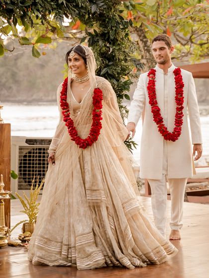 Adorned with traditional red garlands, the couple's ivory outfits create a striking and beautiful contrast, perfect for their beach wedding ceremony.