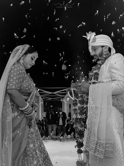 We capture the dramatic and emotional peak moments of your wedding day. This black and white photograph shows the bride and groom during the Varmala ceremony, framed by fireworks and smoke for a truly cinematic feel.
