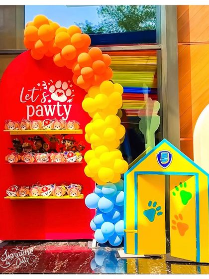 A 'Let's Paw-ty' themed display for party favours, decorated with a colourful balloon garland and a doghouse prop.