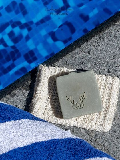 A minimalist, top-down shot of a bar of soap resting by a pool. The strong contrast between the blue water, grey concrete, and striped towel creates a modern, graphic look.