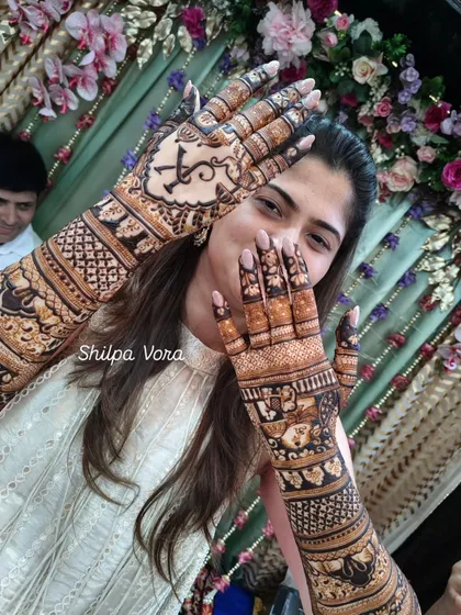 A happy bride showing off her full arm bridal mehndi. The joy on her face is the best reward for my work.