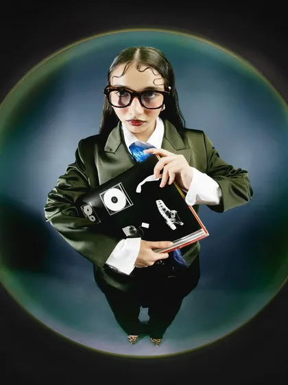 The model holds a book, adding a narrative layer to this experimental portrait. The glasses and serious expression play with the 'geek chic' trope through an avant-garde lens.