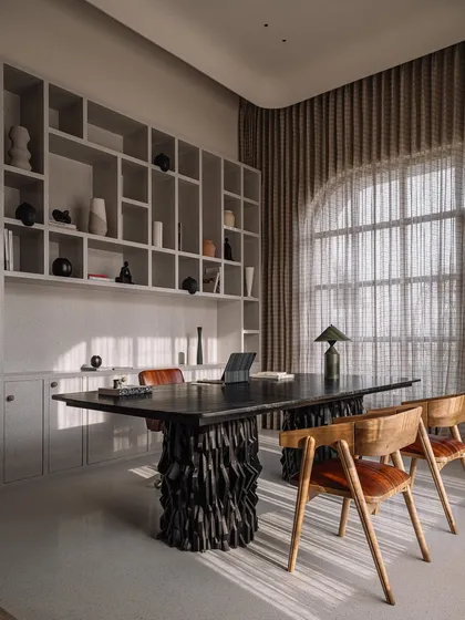 This home office features a commanding desk with a hand-carved, sculptural base. The dark, textured wood provides a powerful contrast to the light-filled room and clean lines of the surrounding built-in shelving.