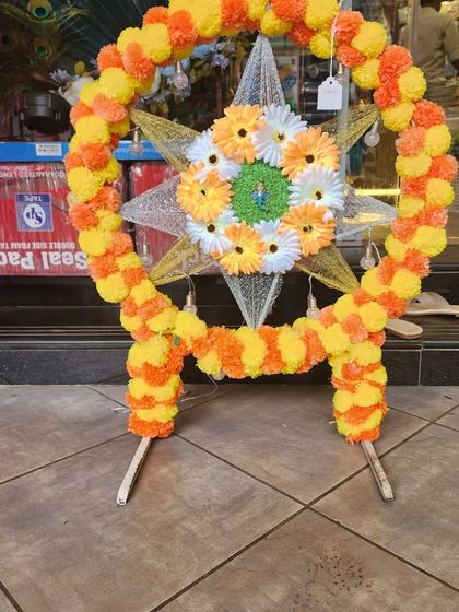 A unique star-shaped Ganpati frame decorated with yellow and orange marigold garlands. This is a creative and modern take on the traditional makhar.