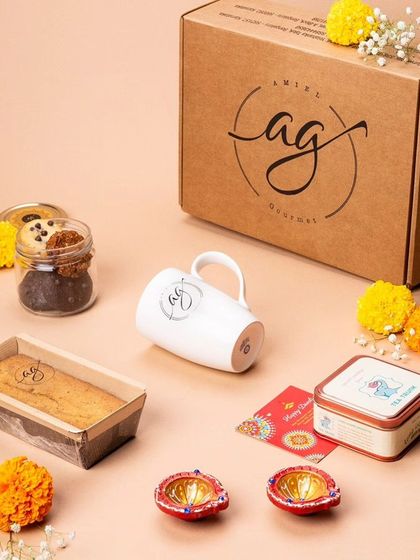 An unboxed view of one of my Diwali hampers. It includes a tea cake, a jar of cookies, an AG mug, a tin of tea, and festive diyas, all ready to be packed into a beautiful gift box.