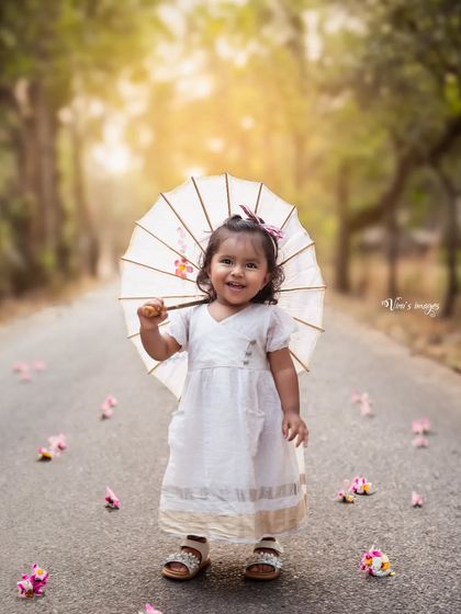 A walk in the park with a pretty parasol. This adorable toddler portrait captures a happy smile as flower petals fall, creating a whimsical and charming outdoor scene.