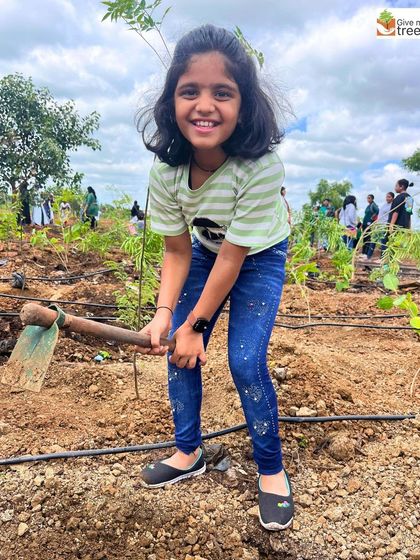 A young participant at the EXL plantation drive in Pune smiles for the camera, hoe in hand. We encourage families to join our corporate events.