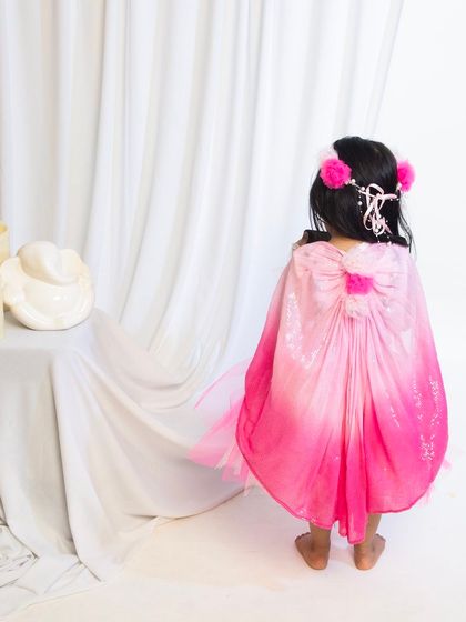 The back view of a child in a pink butterfly or fairy costume with a large bow.