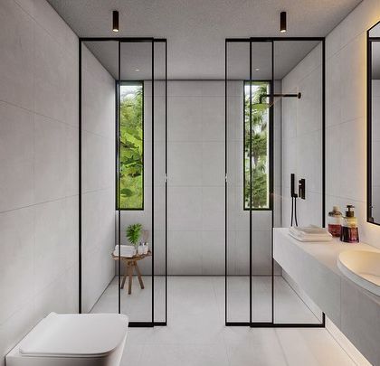 This minimalist bathroom in the Vagator Villas uses glass partitions to create separate zones for the shower and toilet. The design maintains an open feel, with windows bringing in views of the lush Goan landscape.
