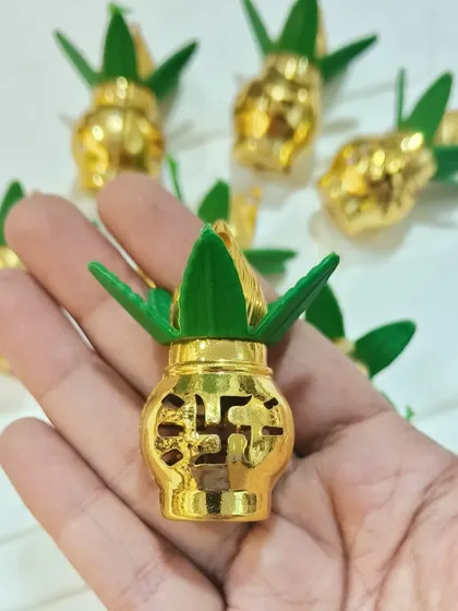 This miniature golden kalash with green leaves is a perfect decorative add-on for pooja platters and festive arrangements. The intricate design includes a swastika symbol for an auspicious touch.