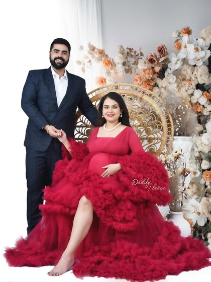A classic couple's portrait featuring a vibrant magenta ruffled gown. The mother-to-be is seated while her partner stands beside her, creating an elegant and colorful memory.