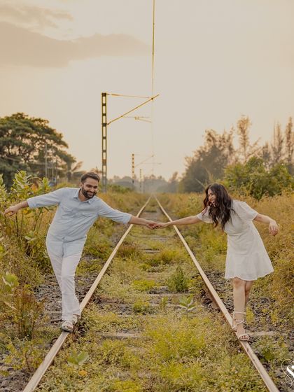 Balancing together, hand in hand. This full-length shot captures the fun and teamwork in their relationship, set against the rustic beauty of the railway tracks.