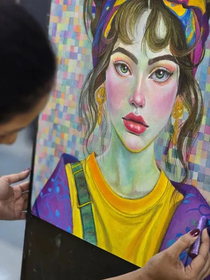 A close-up shot of the artist's hand as she blends colors on the portrait, demonstrating the tactile nature of working with oil pastels.