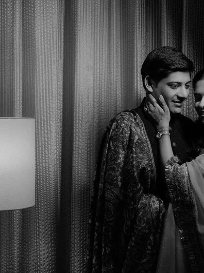 A timeless black and white portrait. The soft light from the lamp and the bride's gentle touch on his cheek create a quiet, romantic atmosphere that feels both classic and intimate.