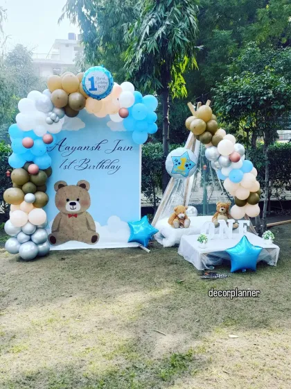 A wider view of the outdoor teddy bear party, showing a large personalized backdrop with a balloon arch, complementing the smaller cabana setup. This is great for larger garden parties.